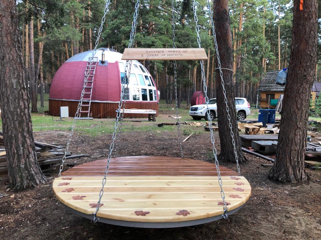Подвесные круглые деревянные качели на фоне купольного дома
